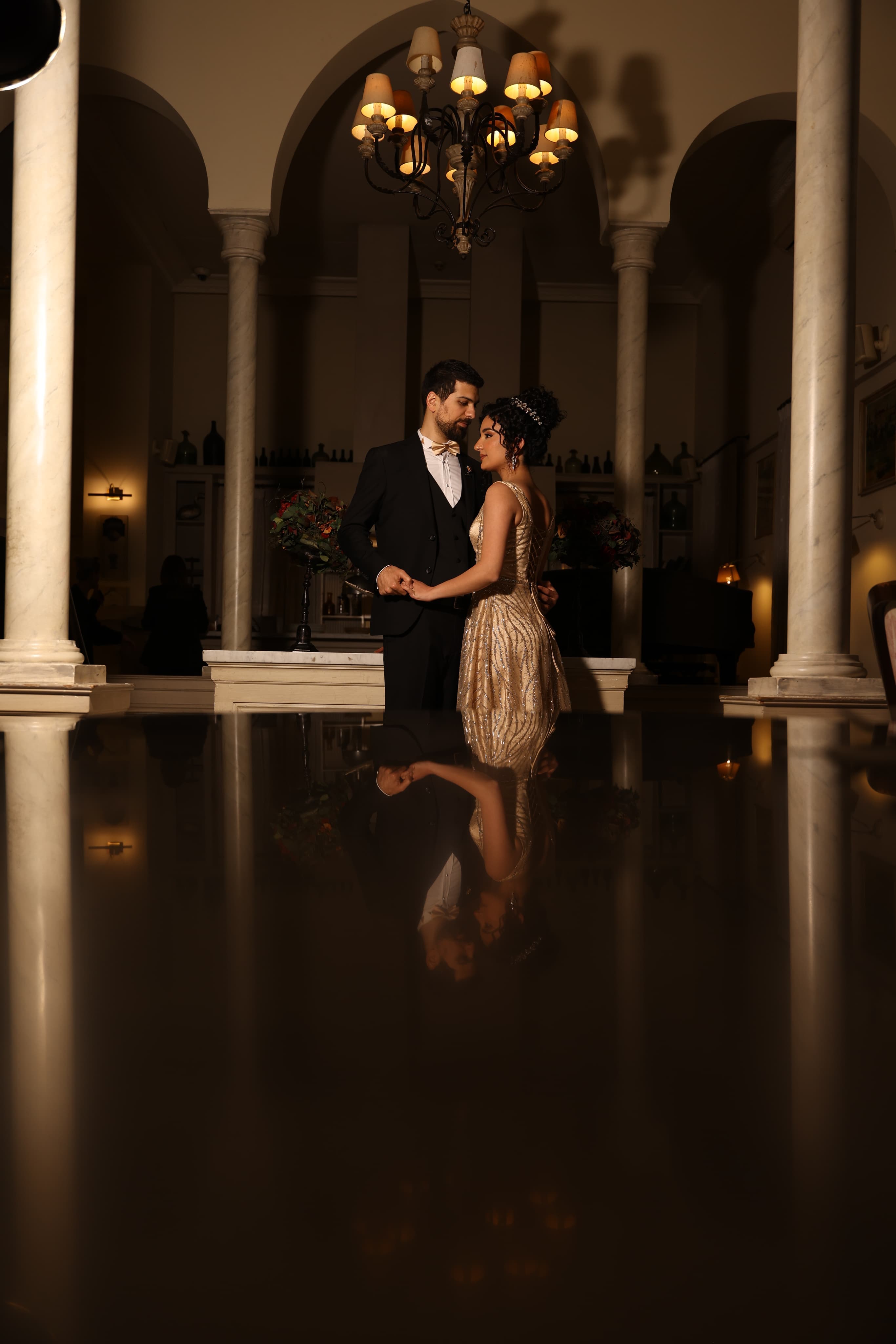 Freddy and Tatiana beneath a chandelier, reflected in a piano